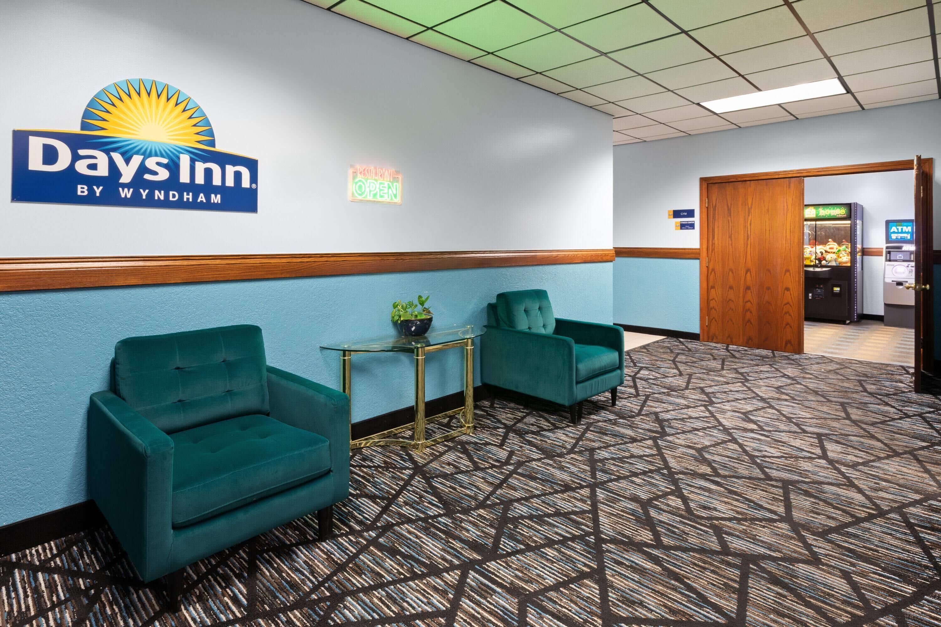 A Days Inn by Wyndham lobby with teal armchairs, a small table with a plant, and a patterned carpet.