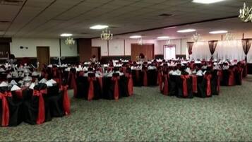 Un salón de banquetes con mesas redondas cubiertas con manteles negros y cintas rojas, dispuestas en filas.