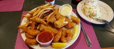 Ein Teller Fish and Chips mit Zitronenspalten und zwei Soßen.