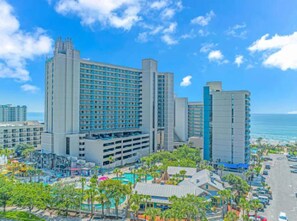 A large hotel with multiple floors, a pool area, and a view of the ocean.