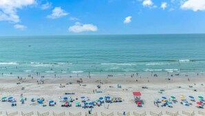 A beach with umbrellas and people, a clear sky, and calm water. - Sand Dunes 2451 (Myrtle Beach)