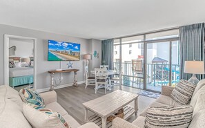 En stue med sofa, sofabord, fjernsyn og en balkon med swimmingpool.