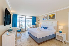 A hotel room with a bed, a desk, a chair, a TV, and a balcony with blue curtains.