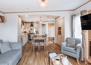 A modern living room with a sofa, a coffee table with books and cups, a fireplace, and a TV mounted on the wall. - 2 bedroom accommodation in Bridgnorth (Bridgnorth)