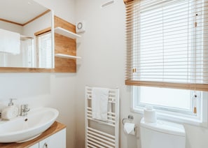 A bathroom with a white sink, wooden shelves, a towel rack, a toilet, and a window with blinds. - 2 bedroom accommodation in Bridgnorth (Bridgnorth)