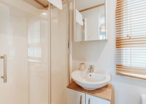 A modern bathroom with a glass shower enclosure, a white sink with a wooden countertop, and a mirror above the sink.