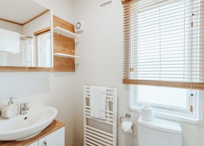 A bathroom with a white sink, wooden shelves, a towel rack, a toilet, and a window with blinds. - 2 bedroom accommodation in Bridgnorth (Bridgnorth)
