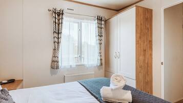 A bedroom with a bed, a radiator, a wardrobe, and a window with curtains.