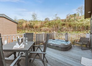 A deck with a hot tub, a table with chairs, and a view of a natural landscape.