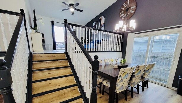 Una escalera con balaustres negros y peldaños de madera que conduce a un comedor con una mesa y sillas.