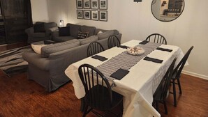 Un salon moderne comprenant un coin repas, des canapés gris, un grand miroir et des tableaux encadrés accrochés au mur.
