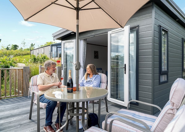 A couple seated at an outdoor table with a large umbrella, a bottle of champagne, and a glass of wine.