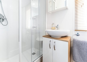 A modern bathroom with a glass shower enclosure, a white sink with a wooden countertop, and a mirror above the sink.