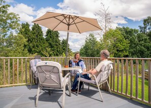 Eine Terrasse mit zwei Stühlen, einem Tisch, einem Sonnenschirm und einer Weinflasche.