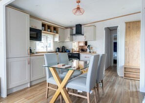 Une cuisine moderne avec des meubles blancs, une table à manger en verre et un plancher en bois.