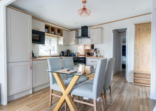A modern kitchen with white cabinets, a glass dining table, and a wooden floor.