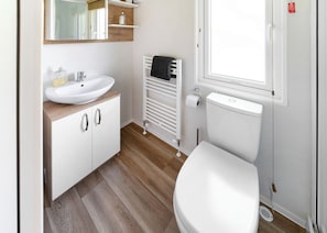 A compact bathroom with a white sink, a toilet, a mirror, and a window.