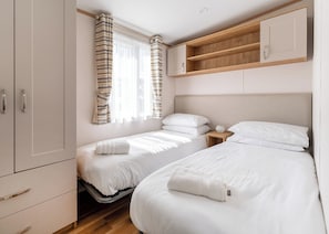 A bedroom with two beds, a wardrobe, a bedside table, and a window with curtains.