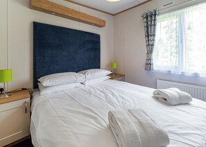 Ein ordentlich bezogenes Bett mit weißen Leinen, ein Holz-Kopfteil, ein Nachttisch mit einer Lampe und ein Fenster mit Vorhängen.