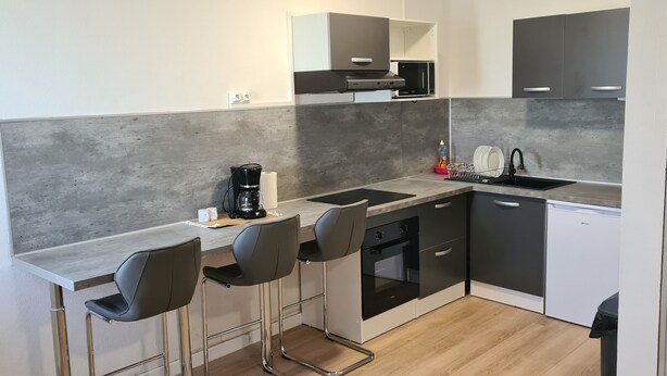 A compact kitchen with a microwave, coffee maker, and a sink. There are three bar stools and a small oven. - Fully furnished and air-conditioned apartment (Les Abymes)