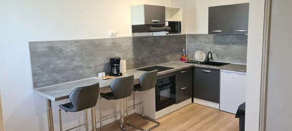 Compact kitchen with oven, sink, and dishwasher, plus a coffee maker and bar stools.