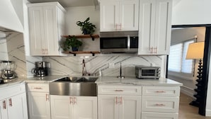 Una cocina moderna con armarios blancos, un lavamanos de acero inoxidable, un microondas, un tostador y una cafetera.