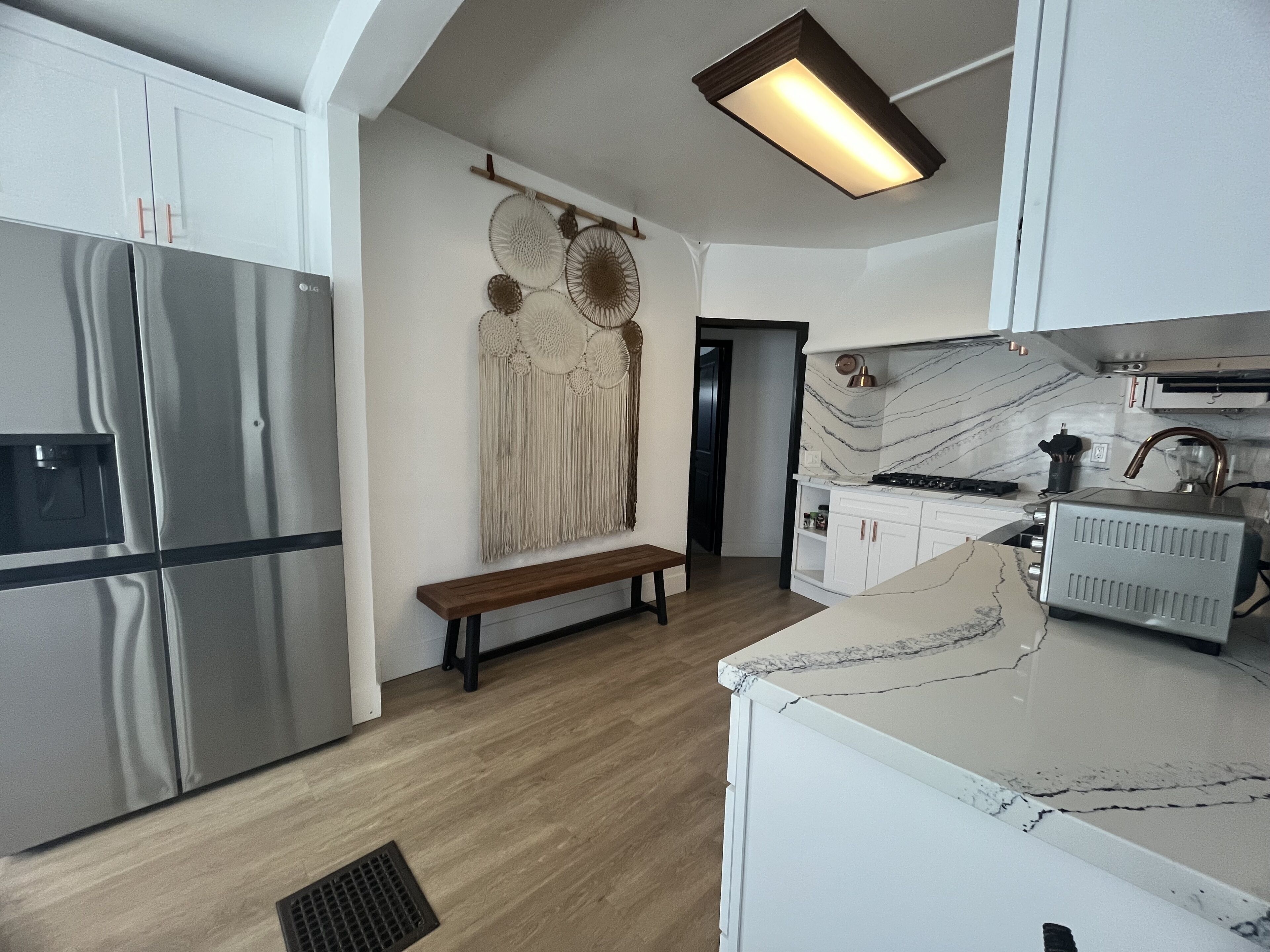 Eine moderne Küche mit weißen Schränken, einem Edelstahl-Kühlschrank, einer Marmorarbeitsplatte und einem eingebauten Ofen.