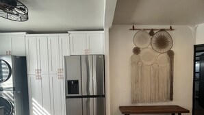 Una cocina con armarios blancos, un refrigerador de acero inoxidable, un banco de madera y un adorno en la pared.