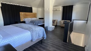 Una habitación de hotel moderna con dos camas, un ventilador de techo, cabeceros de madera y piso de madera oscura.