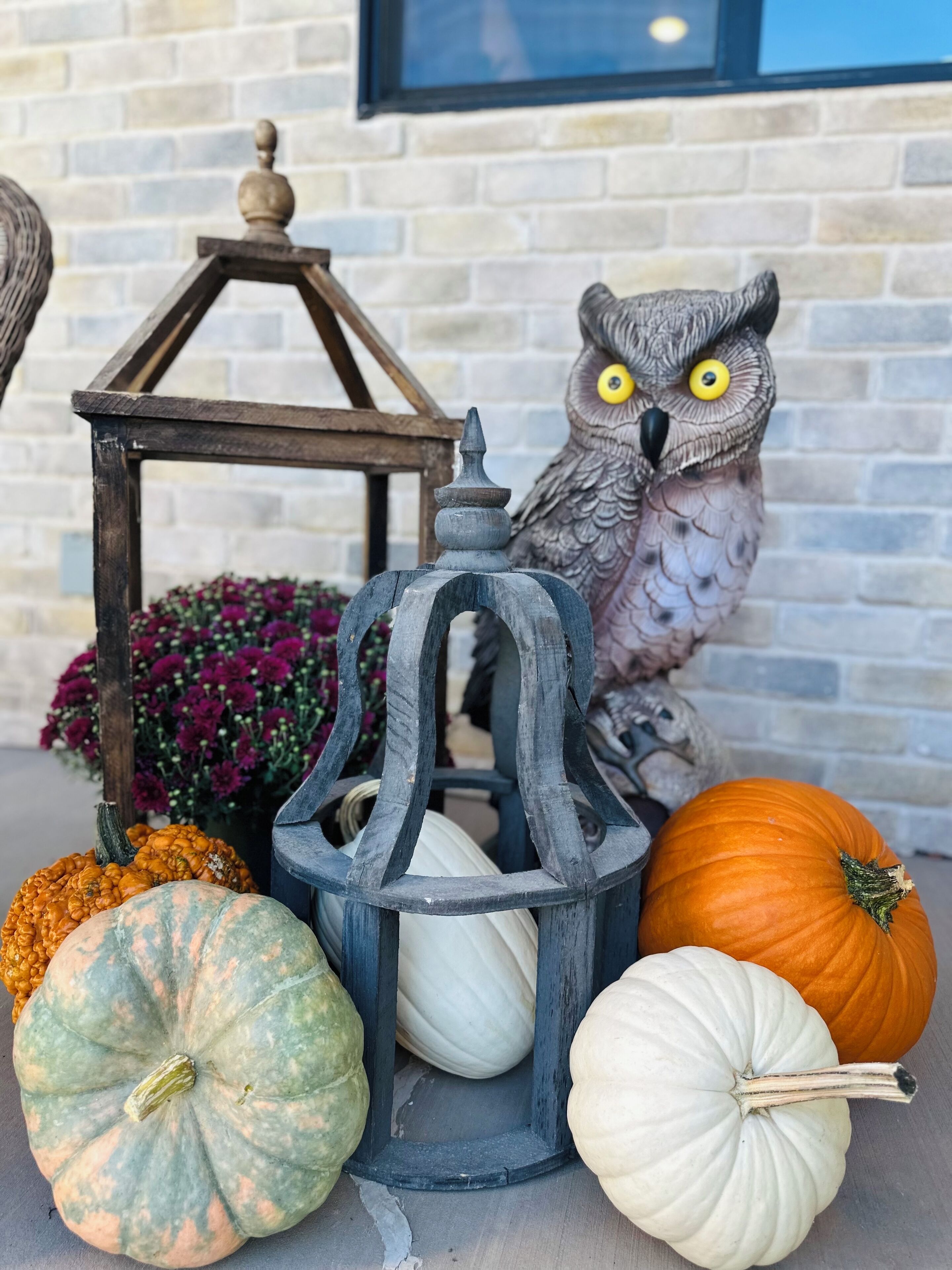A decorative lantern, a carved owl, and pumpkins on a table.