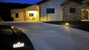A residential property with a paved driveway, a stone exterior, and a well-lit entrance.