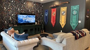 A living room with a television displaying 'Harry Potter and the Sorcerer's Stone', a sofa, a coffee table, and a wall decorated with Harry Potter banners.
