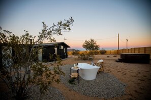 A desert landscape with a small wooden cabin, a white bathtub, and a wooden deck. - The Sage Retreat (Landers)