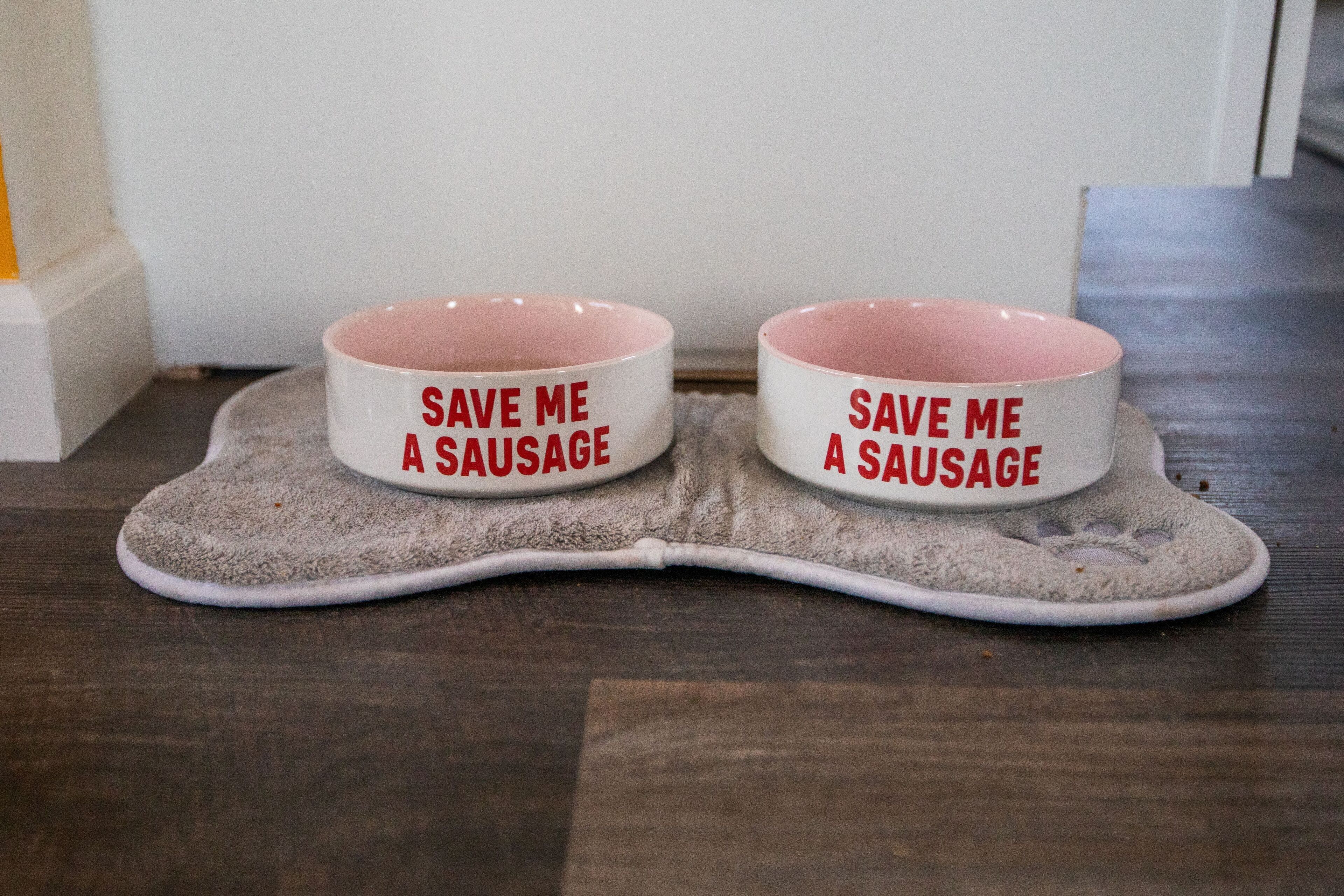 Two pet bowls with the text "SAVE ME A SAUSAGE" on a mat.