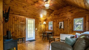 A cozy cabin interior with wooden walls, a dining area, a sofa, and a fireplace.