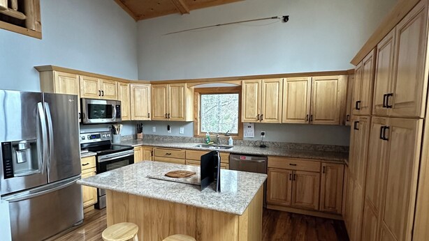 A modern kitchen with wooden cabinets, stainless steel appliances, and a granite countertop island with stools. - Minnesota lakefront home/cabin near Tower and Ely, close to Bear Head State Park (Ely)