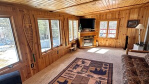 A wooden cabin interior with a fireplace, a television, and a large rug with animal prints. - Minnesota lakefront home/cabin near Tower and Ely, close to Bear Head State Park (Ely)
