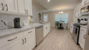 A modern kitchen with white cabinetry, a granite countertop, and a dining area with a table and chairs. - Minutes from Tulsa!  Come relax with the family in this pet friendly home  (Owasso)