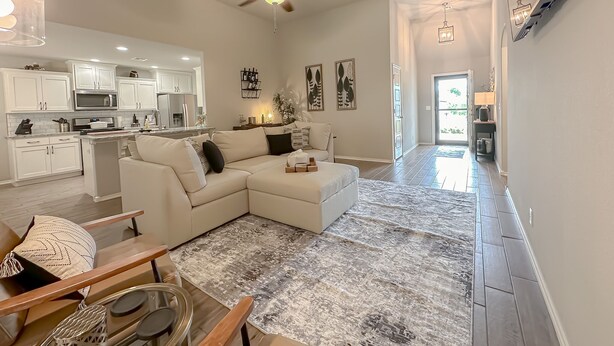 A modern living room with a sectional sofa, a dining area with a table and chairs, a kitchen with white cabinets, and a ceiling fan. - Minutes from Tulsa!  Come relax with the family in this pet friendly home  (Owasso)