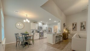 A modern kitchen with white cabinets, a central island, and a dining area with a table and chairs. - Minutes from Tulsa!  Come relax with the family in this pet friendly home  (Owasso)
