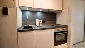 Cocina compacta con horno integrado, pileta y encimera con una tetera y un rodillo de toallas de papel.