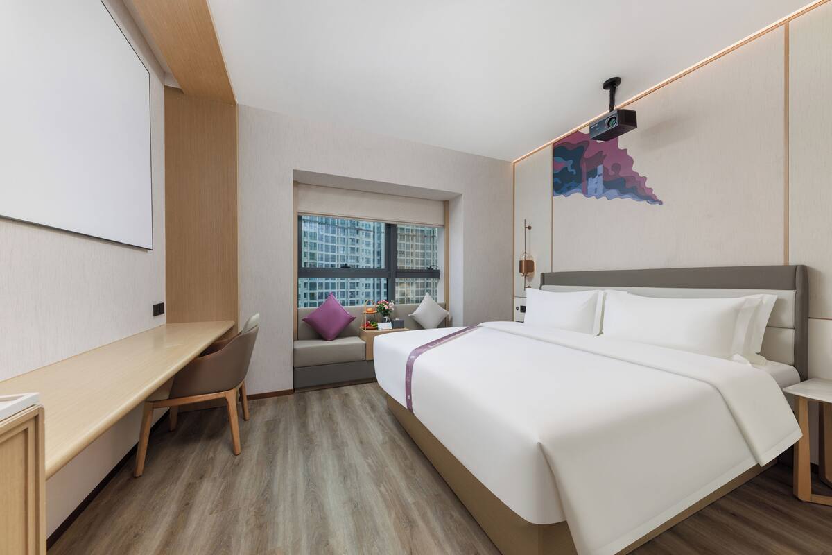 Ein modernes Hotelzimmer mit einem großen Bett, einem Schreibtisch und einem Fenster mit Blick auf die Stadt.
