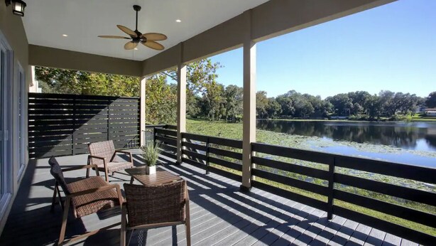 A covered outdoor area with a view of a lake, wooden furniture, and a ceiling fan.