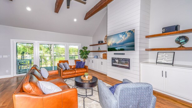 A spacious living room with a leather sofa, a coffee table, and a fireplace. There are large windows offering a view of the outdoors. - The Gallery of Monkey Island [ WITH 28x14 BOAT SLIP] (Monkey Island)