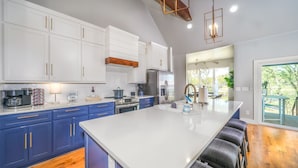 A modern kitchen with white and blue cabinets, stainless steel appliances, and a large island with bar stools. - The Gallery of Monkey Island [ WITH 28x14 BOAT SLIP] (Monkey Island)