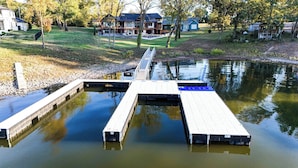 A dock extending into a calm body of water with a grassy bank and houses in the background. - The Gallery of Monkey Island [ WITH 28x14 BOAT SLIP] (Monkey Island)
