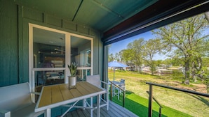 A balcony with a wooden table and white chairs, overlooking a green lawn and trees. - The Gallery of Monkey Island [ WITH 28x14 BOAT SLIP] (Monkey Island)