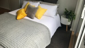 Una cama bien hecha con un plaid gris de punto, ropa de cama blanca y varias almohadas en tonos amarillo y gris.
