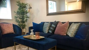 Una sala de estar con un sofá azul, una mesa de centro de vidrio y una alfombra blanca y esponjosa.