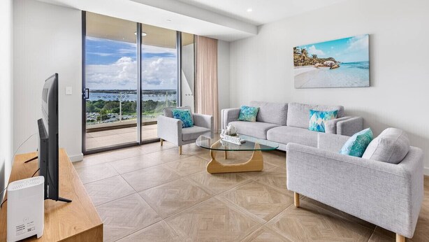 Een moderne woonkamer met een bank, fauteuils, een glazen salontafel en een flatscreen televisie.